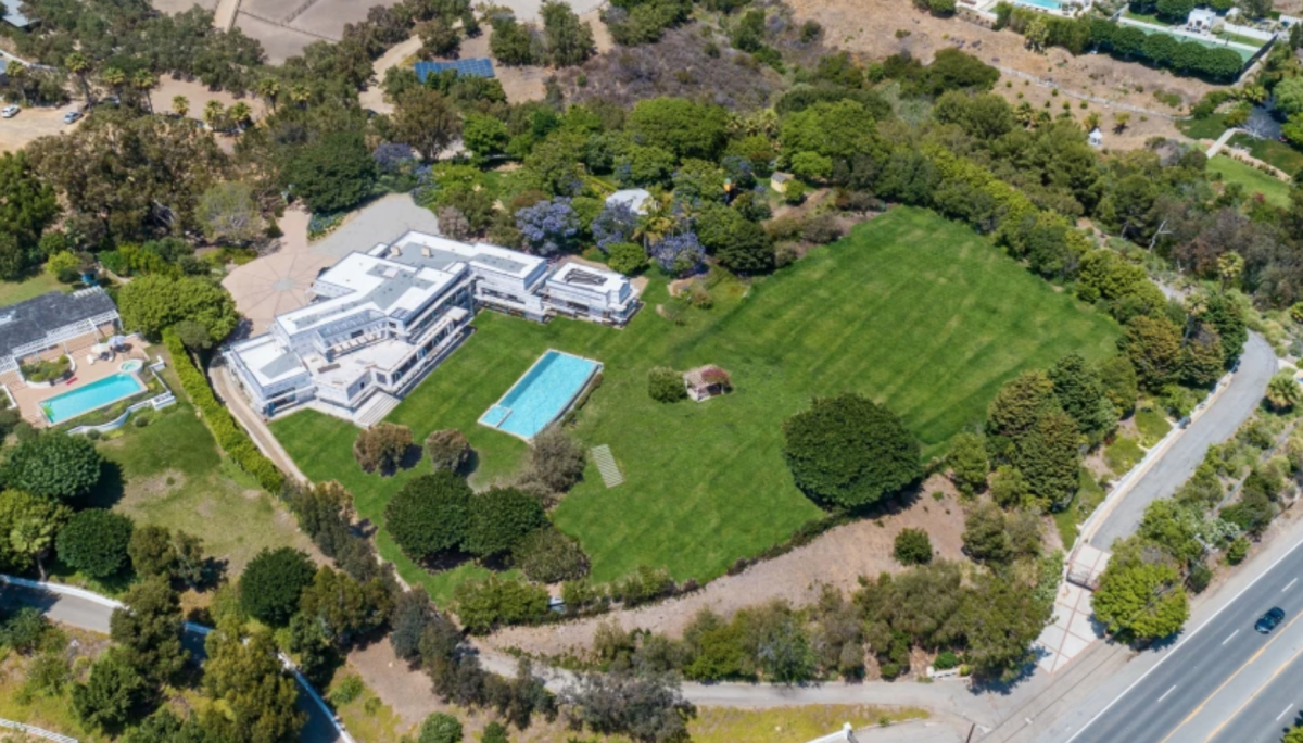 An aerial photo of a large white home with a pool in a big lawn.