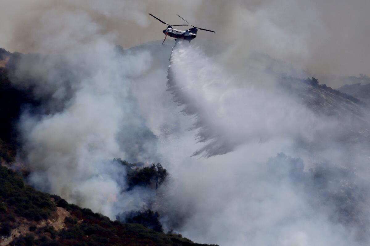 A firefighting helicopter battles the airport blaze, dropping water near Santiago Peak.