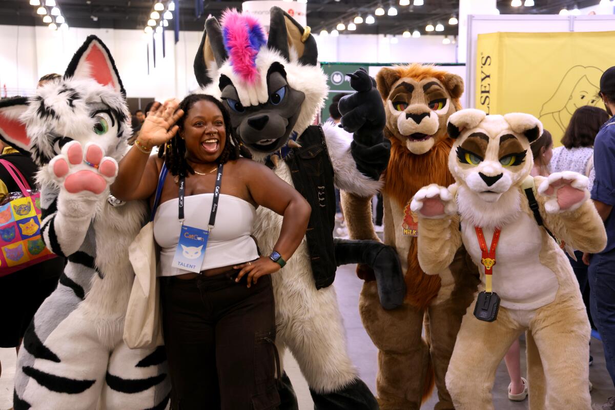 A woman posing with people dressed as cats.