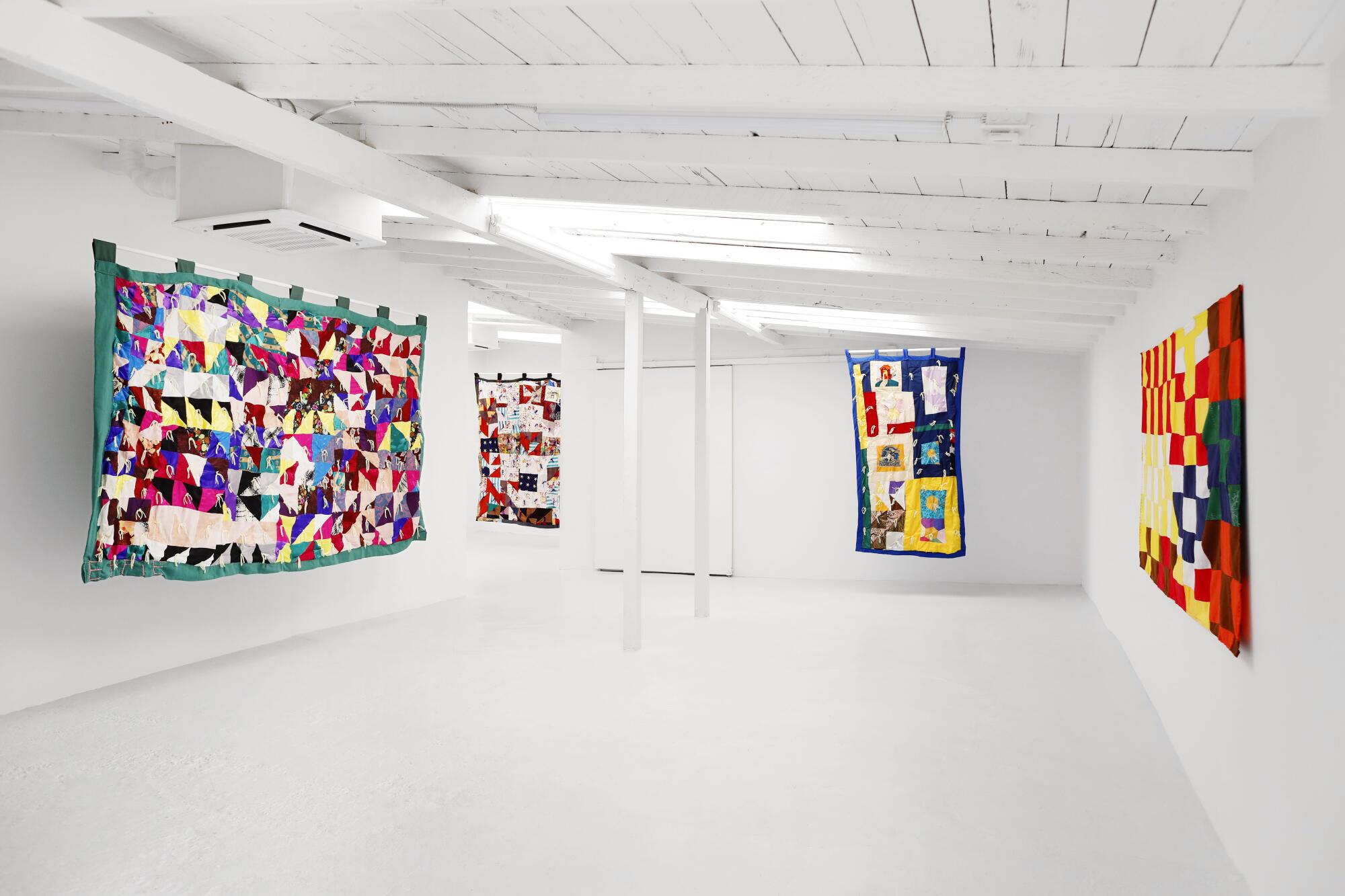 Four colorful quilts hanging on white walls at an art gallery
