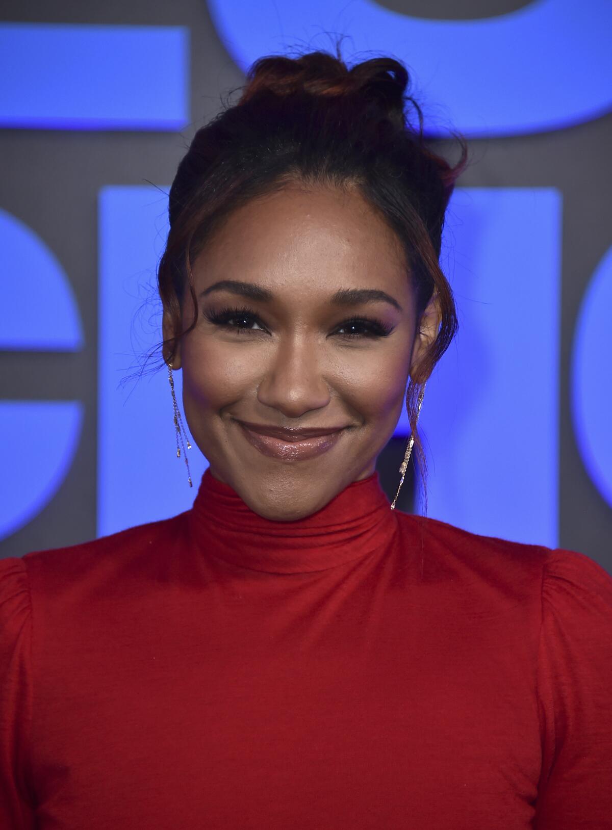 A woman wearing a red turtleneck smiles for cameras at a red carpet event