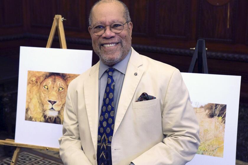 Children's book illustrator Jerry Pinkney poses in front of two of his illustrations Tuesday, July 19, 2016, at City Hall in Philadelphia. As Pinkney was honored by Philadelphia city officials Tuesday, he said his hometown of Philadelphia and African-American history play powerful roles in his career illustrating more than 100 children's books. (AP Photo/Dake Kang)