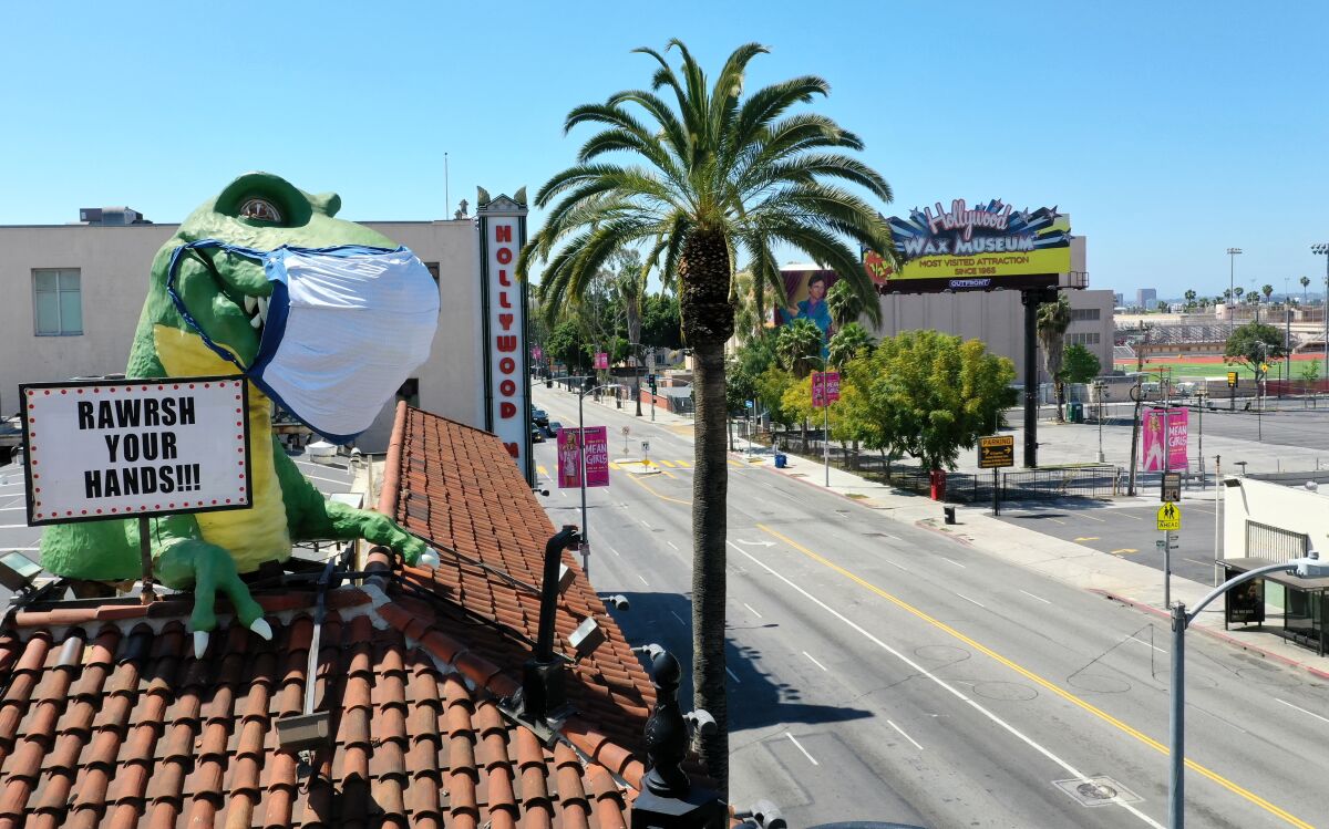 A giant T-Rex wearing a protective mask sends a coronavirus message to a mostly empty intersection of Hollywood Boulevard and Highland Avenue from the top of Ripley's Believe It or Not! Odditorium, which is temporarily closed.