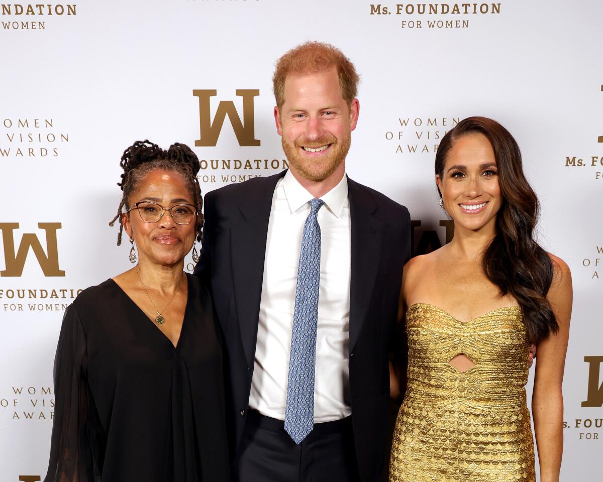 Doria Ragland, left, son-in-law Prince Harry and daughter Meghan Markle stand together, posing for photo, smiling. 