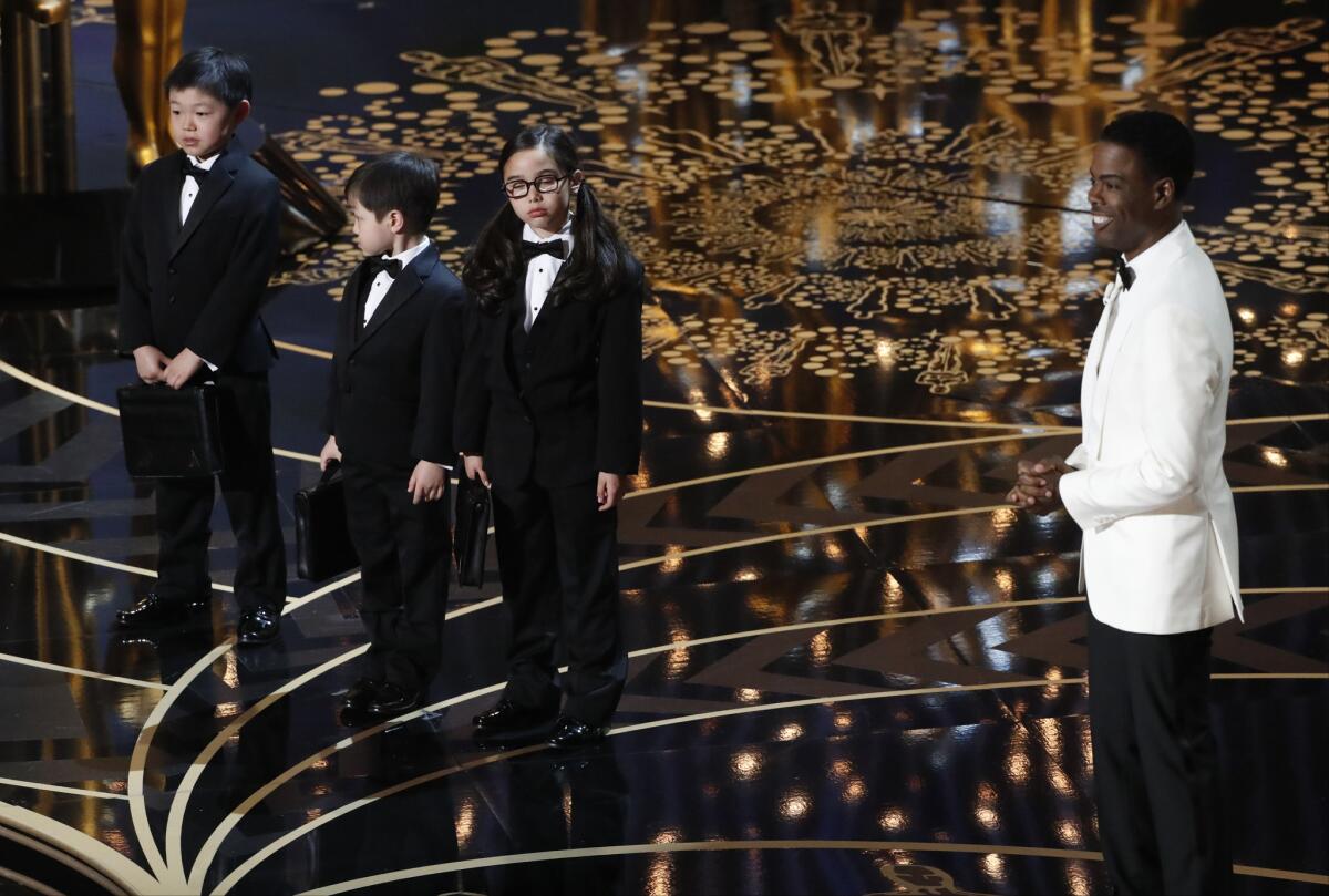 Oscar host Chris Rock, right, introduces three Asian children as PricewaterhouseCoopers accountants.