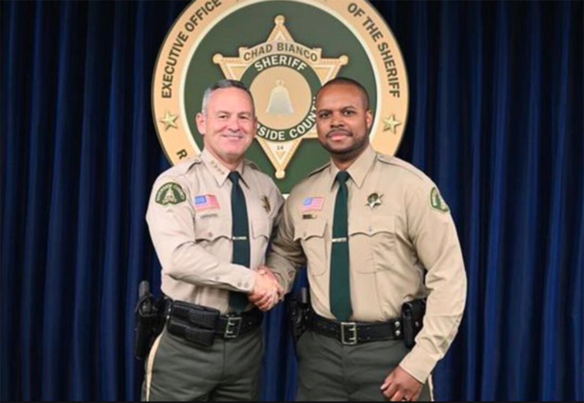 Sheriff and deputy shake hands in front of department shield
