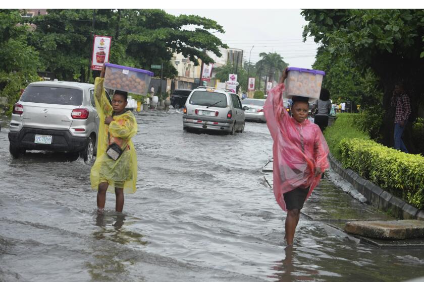 FILE - Women walk along a flooded street after a heavy downpour in Lagos, Nigeria, July 10, 2024. (AP Photos/Sunday Alamba, File)