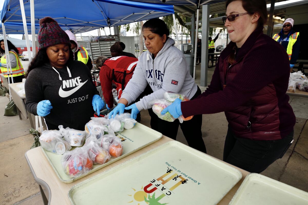 LOS ANGELES CA MARCH 18, 2020 -- Courtney Johnson, Benjula Prasad and Cindy King, left to right, preparing the food kits to be distributed to drivers at Dorsey High School Wednesday morning, March 18, 2020. (Al Seib / Los Angeles Times)