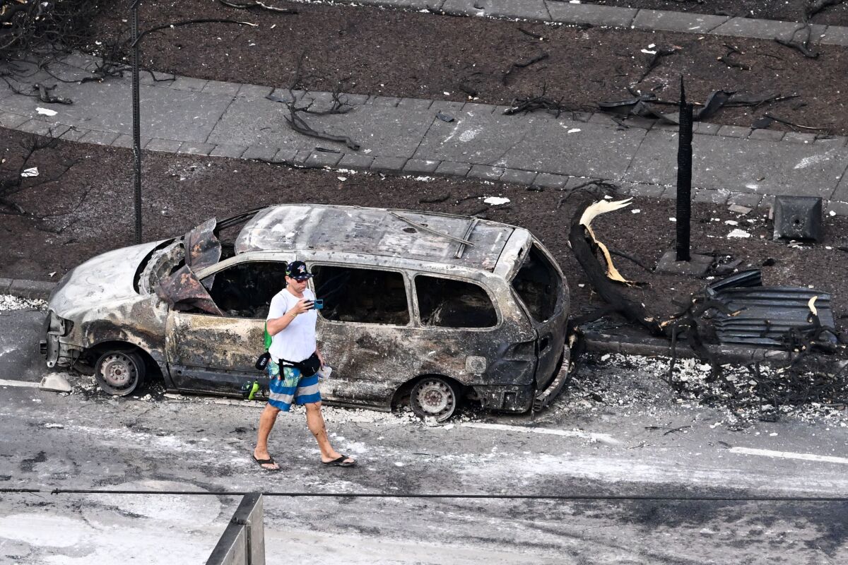 A person walks past a destroyed vehicle.