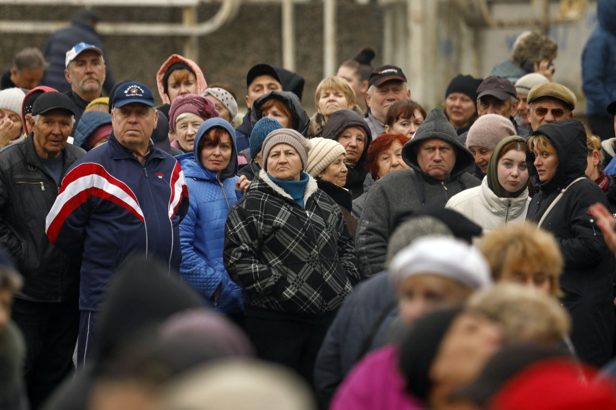A crowd of people standing together, dressed in warm clothing, many wearing hooded jackets 