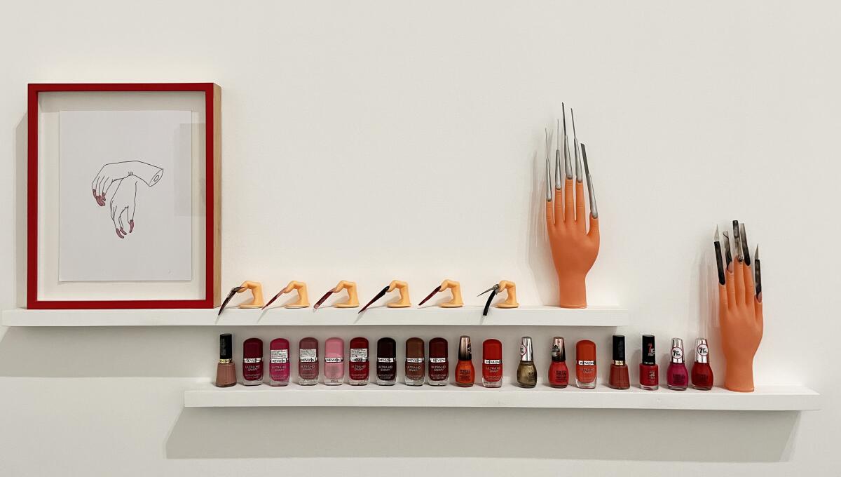 A narrow shelf on a gallery wall features manicure implements and an altered mannequin's hand with blades for nails.