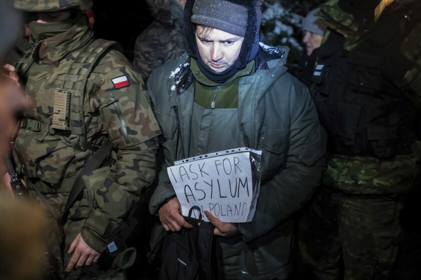 Un solicitante de asilo de Siria que fue detenido por las autoridades fronterizas polacas sostiene un letrero con el mensaje "Pido asilo en Polonia", en Harkawicze, Polonia, el miércoles 1 de diciembre de 2021. (AP Foto/Michal Kosci)