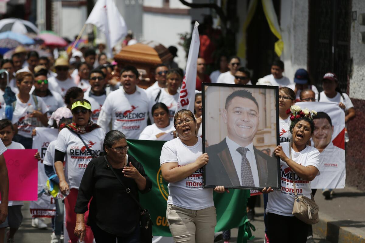 Women carry a poster-size photo of a mayoral candidate during his funeral procession
