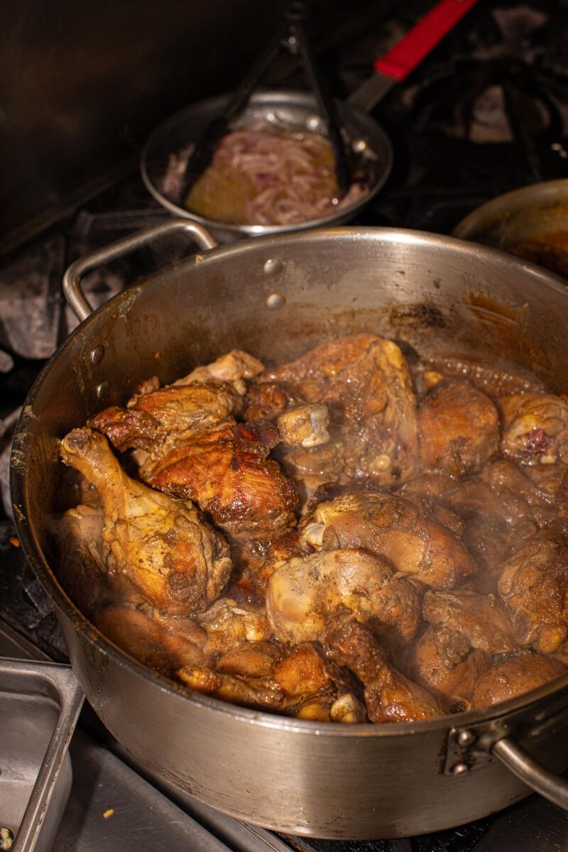 A metal pan full of chicken cooking on a restaurant stove.  
