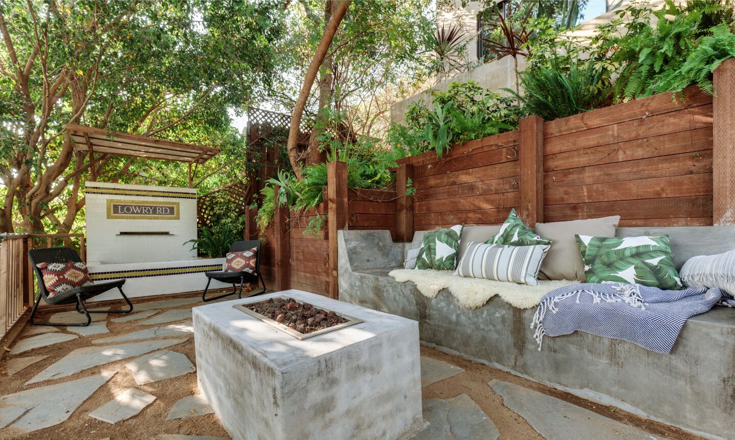 The fire pit with a sitting area nearby and greenery behind a retaining wall.