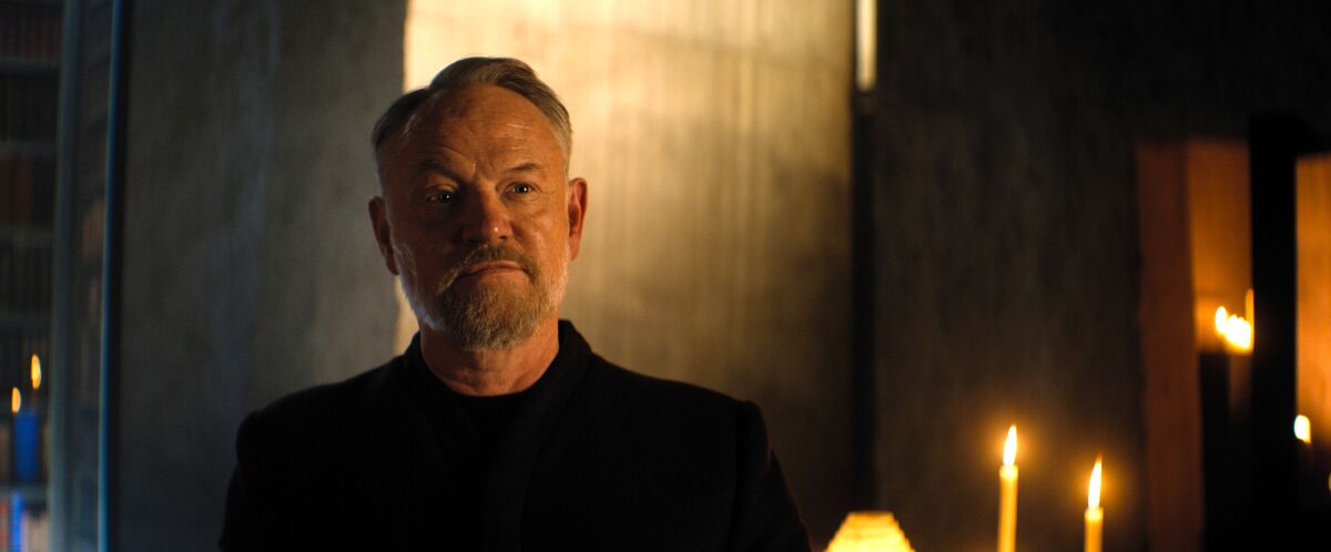 Jared Harris as Hari Seldon in dark clothing with candles lit in the background.