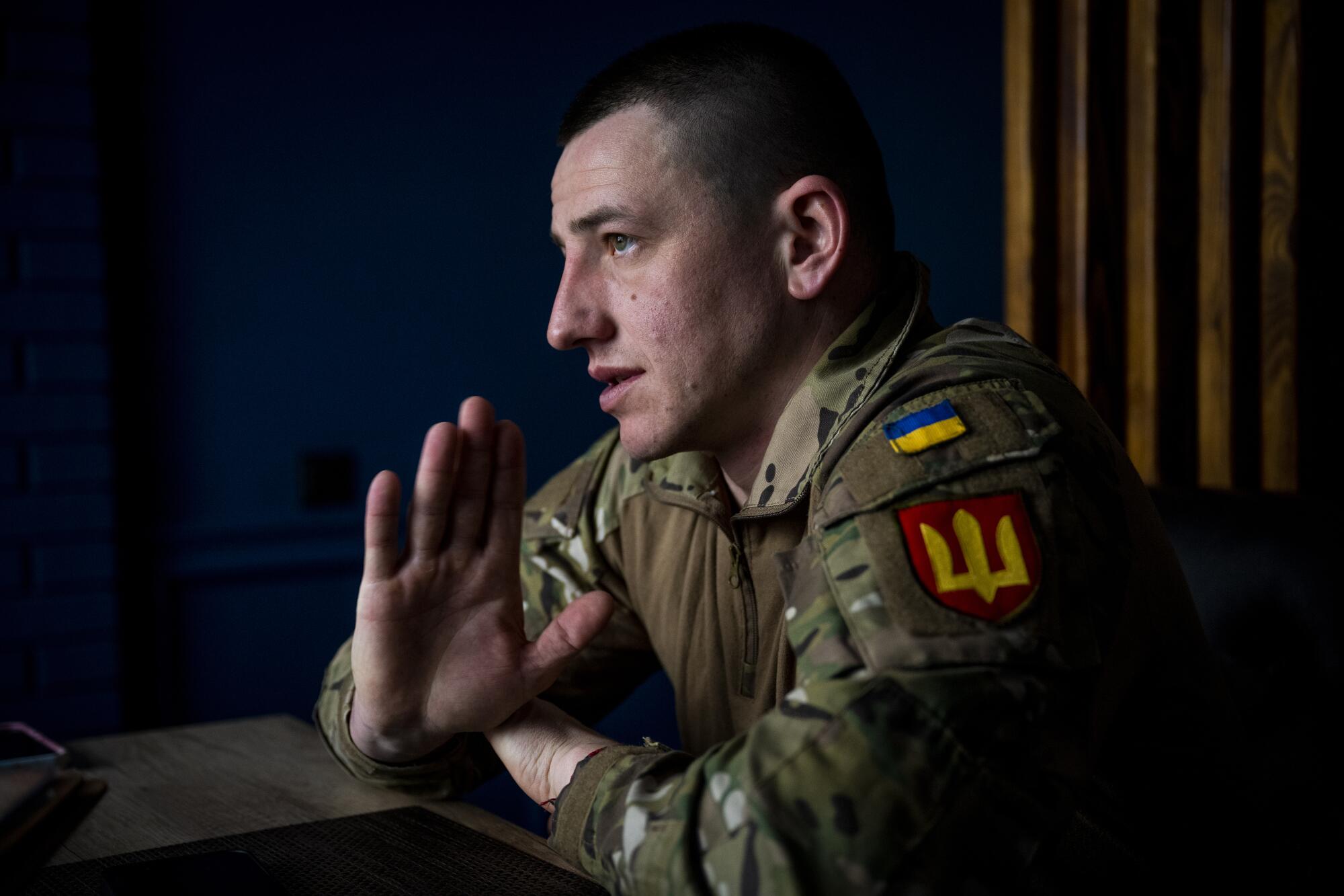 A Ukrainian soldier in uniform raises one hand as he speaks.  