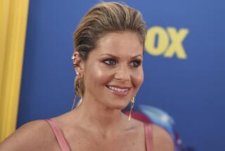 Candace Cameron-Bure with her hair slicked back wearing a pink dress and gold dangling earrings