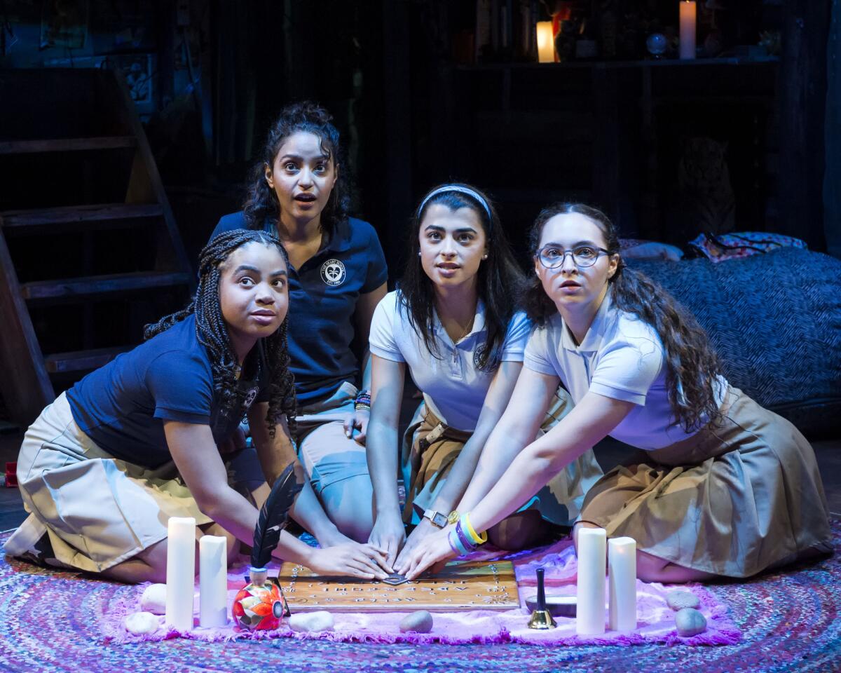 Four teen girls sit on the floor and look up as they surround a Ouija board.