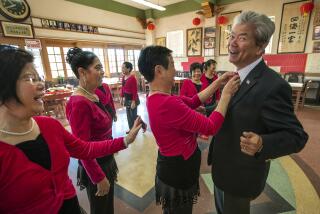 LOS ANGELES, CA-NOVEMBER 6, 2022:Paxton Chew, 70, President of the Lung Kong Tin Yee Association on Broadway in Los Angeles, has his tie adjusted by Hui-Hua Kwan, 73, 2nd from right, a member of the Lung Kong Dancing Group Association as other members look on, during a break from a rehearsal inside the Lung Kong Family Association headquarters on Broadway in Los Angeles. (Mel Melcon / Los Angeles Times)