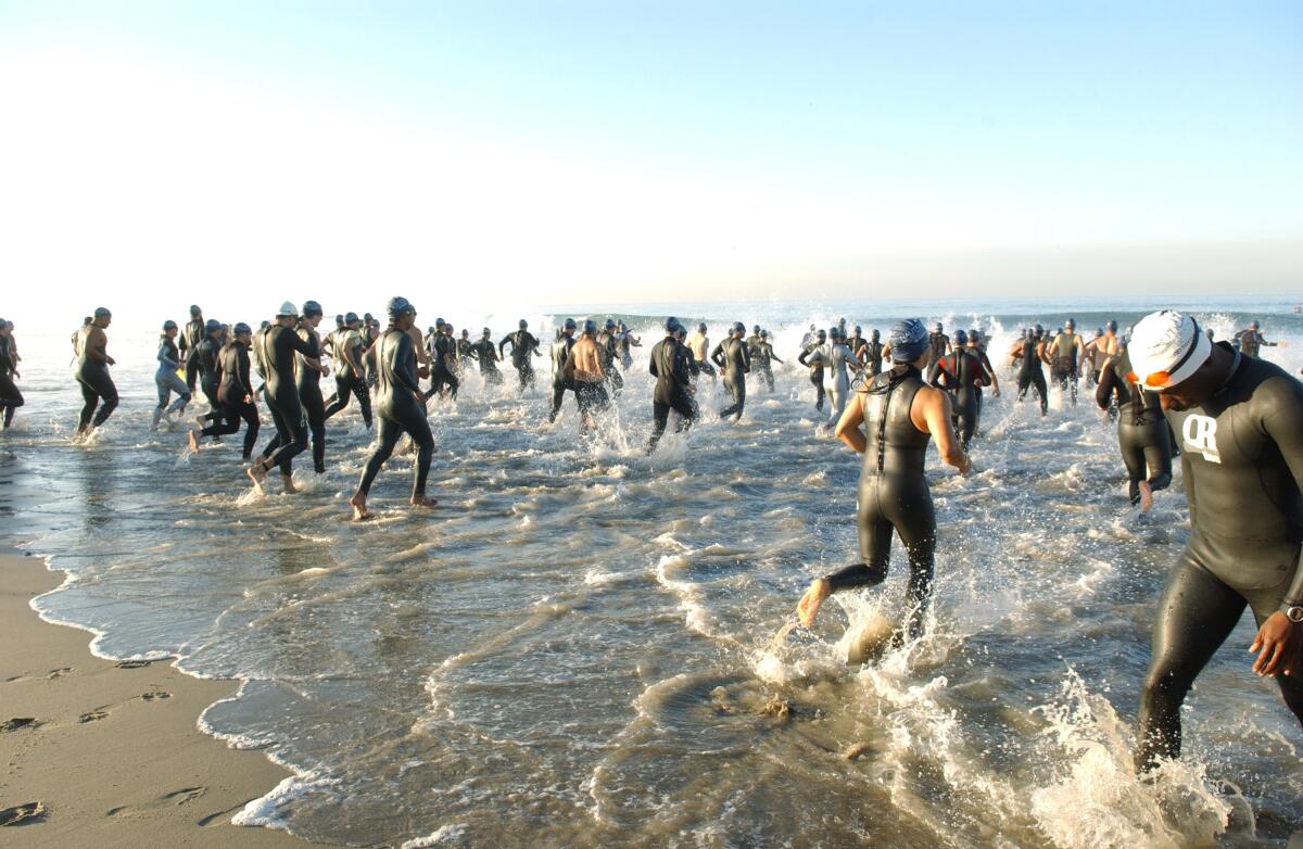 A crowd of people in wetsuits run into the surf at a beach.