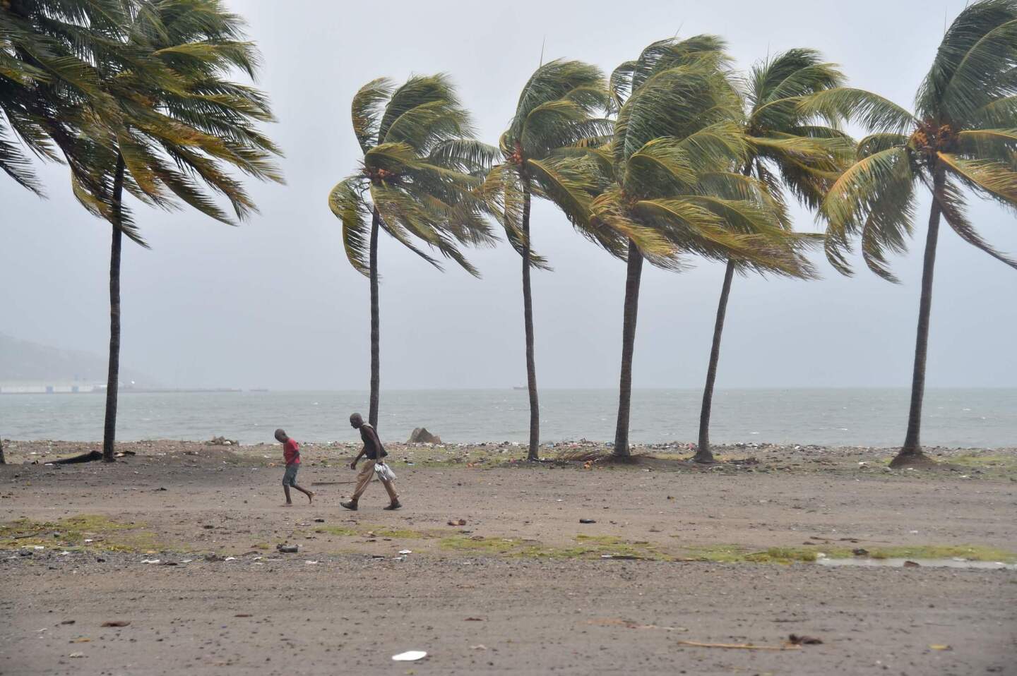 Haitian people walk through the wind and rain on a beach, in Cap-Haitien on September 7, 2017, as Hurricane Irma approaches. Irma was packing maximum sustained winds of up to 185 mph (295 kph) as it followed a projected path that would see it hit the northern edges of the Dominican Republic and Haiti on Thursday, continuing past eastern Cuba before veering north for Florida.