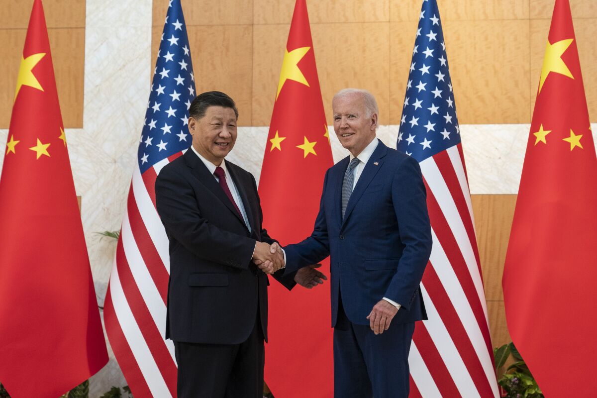 Two men in suit and tie shake hands in front of U.S. and Chinese flags 