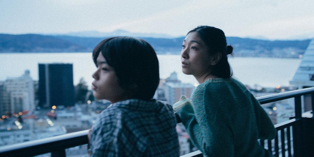 A boy and a woman look over a skyline from a balcony.