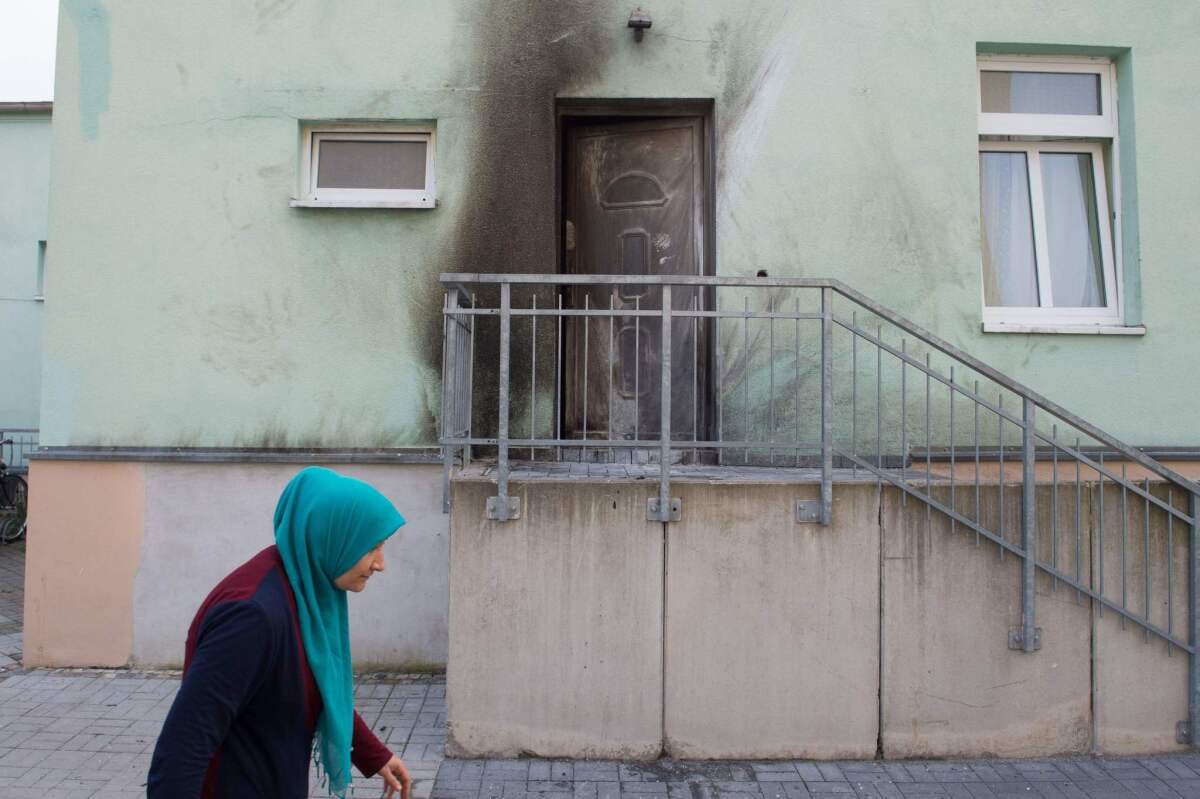 A woman wearing a headscarf walks past the entrance to the Fatih Camii Mosque in Dresden, eastern Germany, where traces of smoke can be seen after a bomb attack.