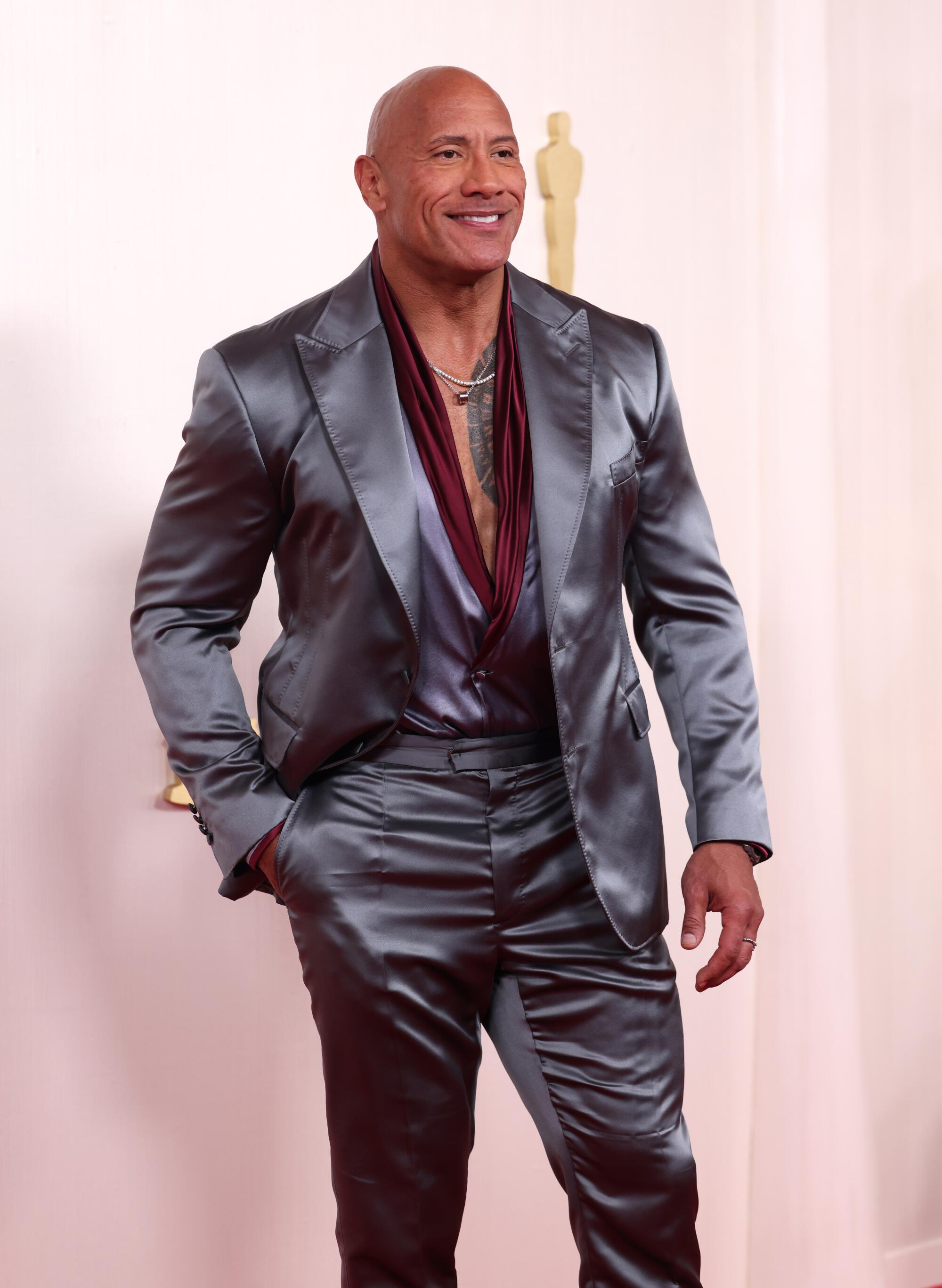 Dwayne Johnson wears a silk silver suit with burgundy trim on his shirt.