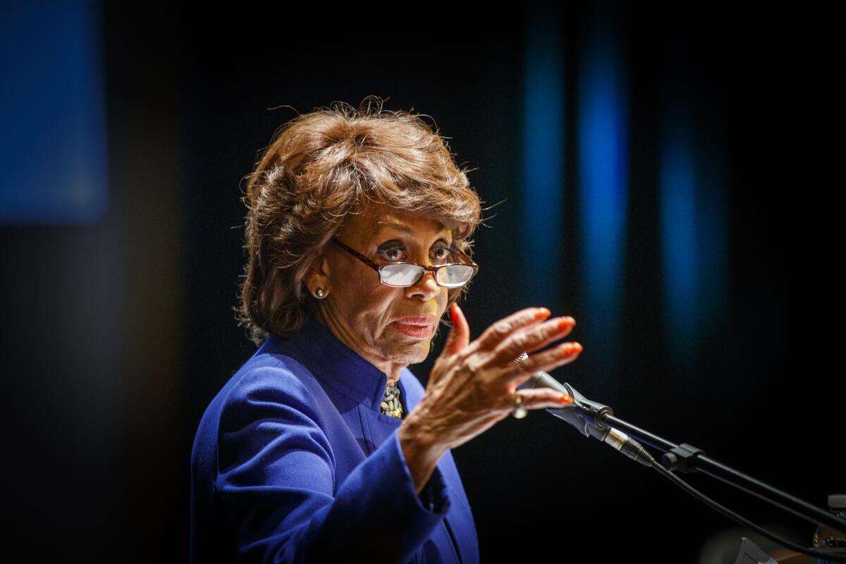 Maxine Waters gestures with one hand as she speaks into a microphone.