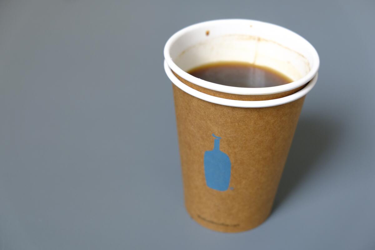 Un vaso de papel de café Blue Bottle Coffee descansa sobre una mesa en el exterior de uno de sus cafés de San Francisco. La cadena con sede en Oakland dice que se deshará de las tazas desechables en dos lugares el próximo año.