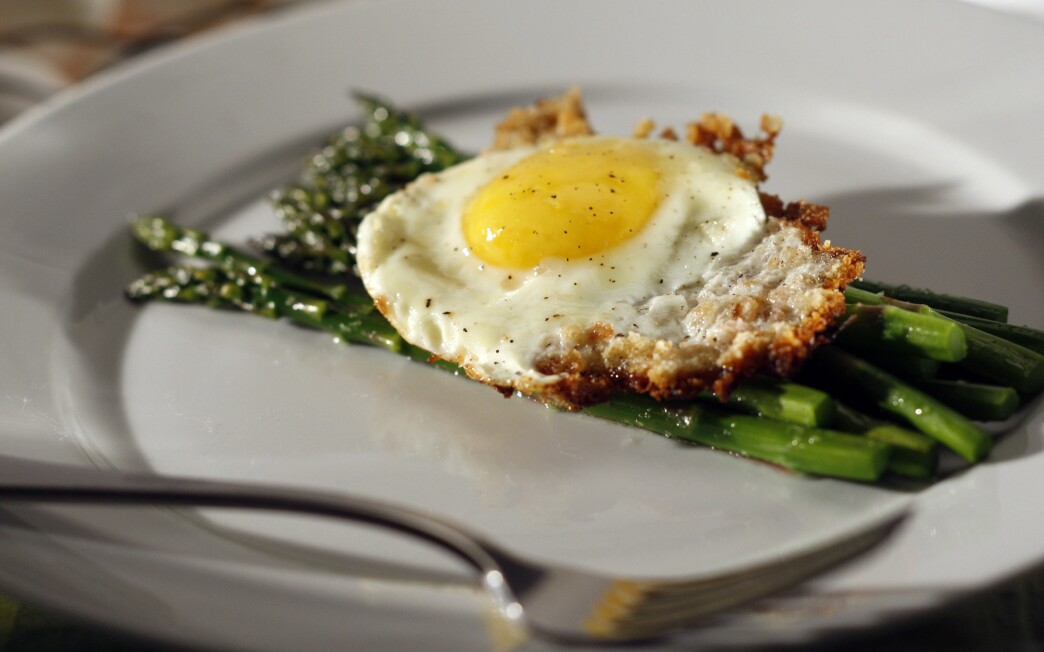A bread crumb-fried egg sits atop a bed of steamed asparagus. 
