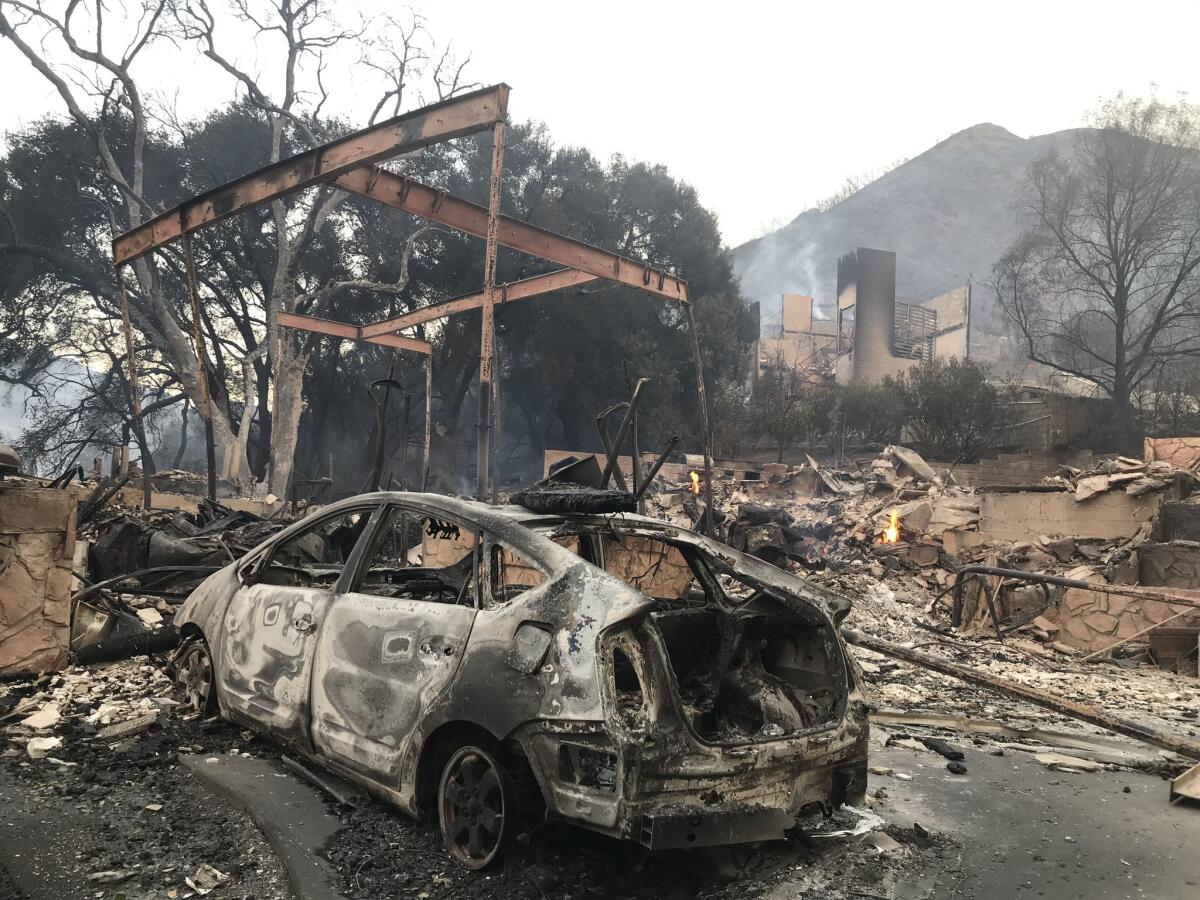 A burned-out car and structures smolder in the wake of the Woolsey fire.