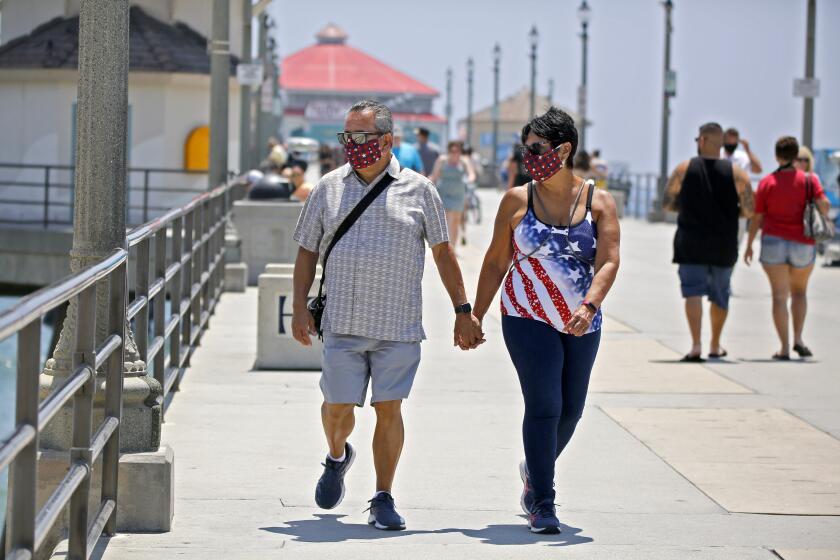 Danny Lopez of Chino Hills and his date Frances Pluma of Norwalk wear face coverings as they stroll on the pier in Huntington Beach on Friday, June 26, 2020.