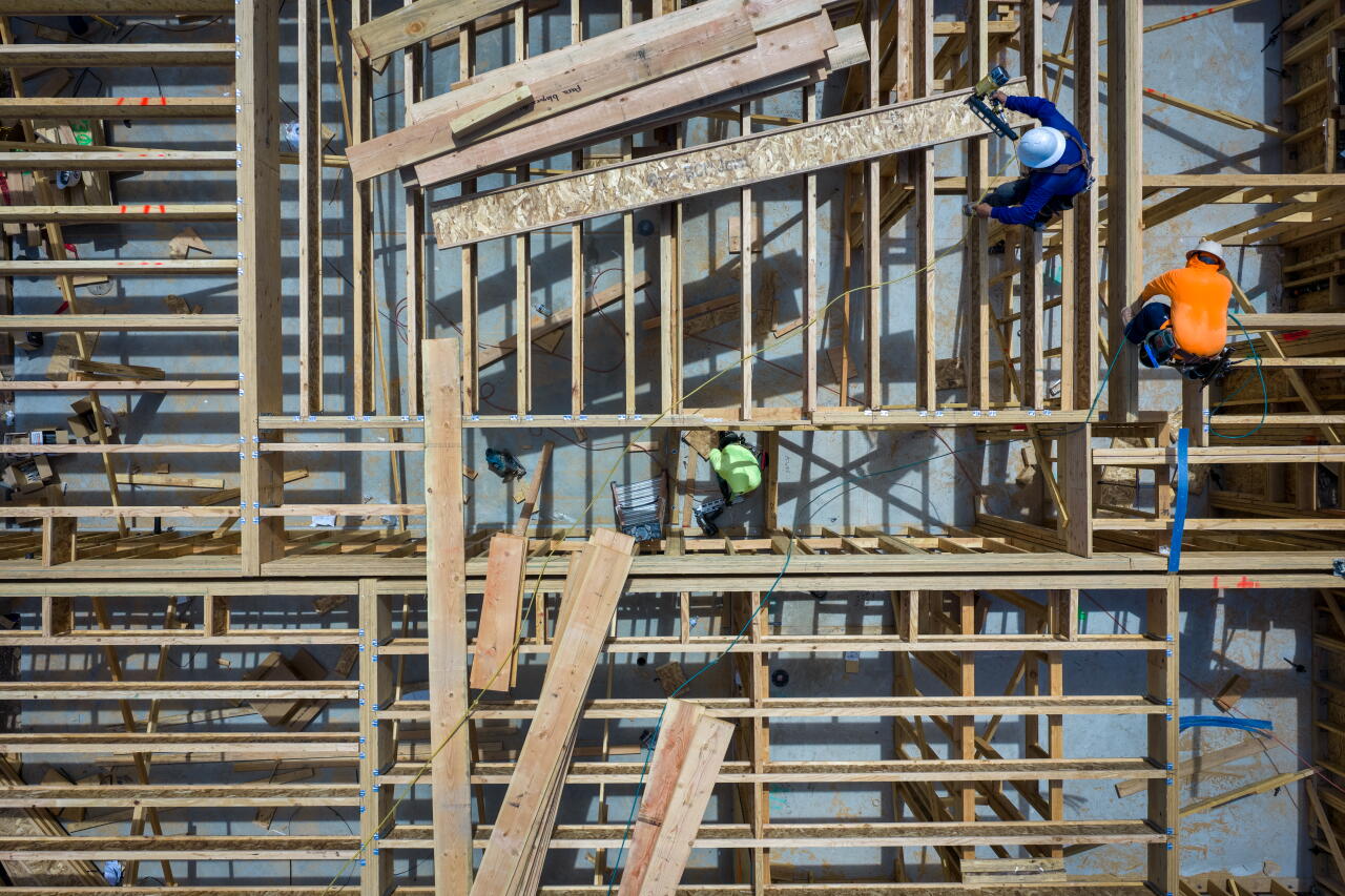 An overhead photo of workers climbing the wood frame of a building under construction.