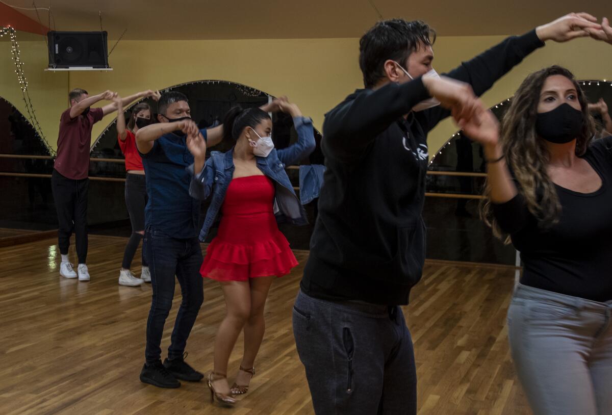 Six people in masks partner-dance inside an L.A. studio. 