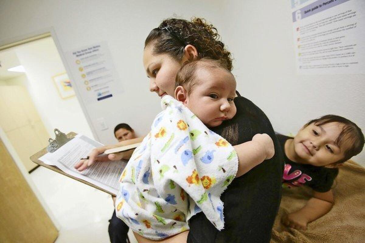 Marisela Garcia, 27, holding 2-month-old son Abraham Angulo, fills out paperwork at Molina Health Clinic in Fontana with her other children, Victor, 11, and 3-year-old Miley. Garcia is currently on Medi-Cal, but her recent marriage means she will no longer qualify for it and must switch to a plan offered through Covered California.