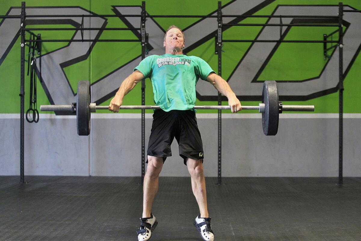 Owner Bryan Wadkins demonstrates how to do a squat and snatch, as part of a CrossFit exercise routine known as Amanda, at his gym CrossFit RXD in Anaheim on Monday. Wadkins is heading to the Olympic Games to compete in CrossFit. He was ranked as one of the fittest out of 5,000 men in his category.