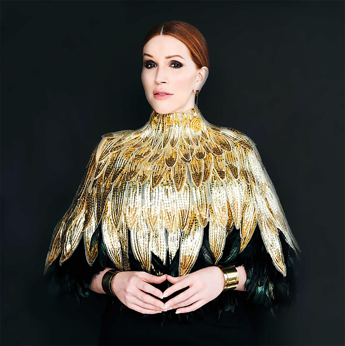 A woman standing in front of a black backdrop dressed in a golden feather pattern.