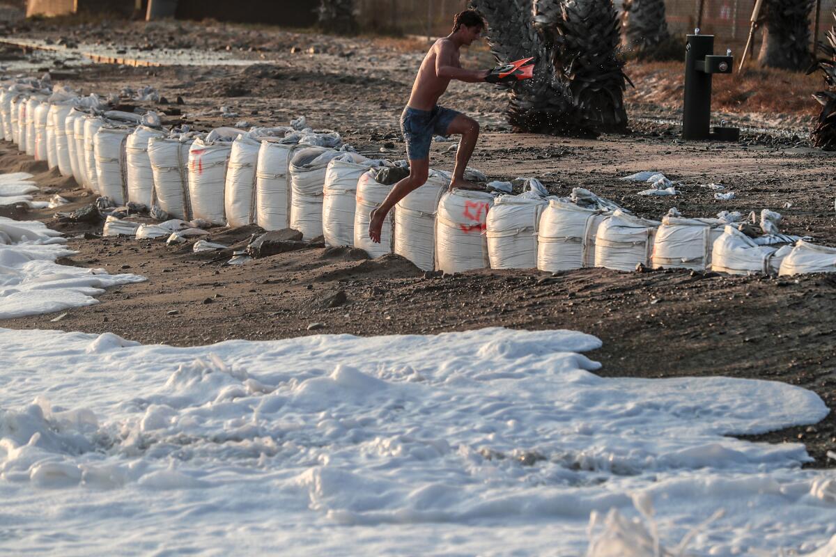 A swimmer jumps over white sandbags as the tide goes toward him at Capistrano Beach. 