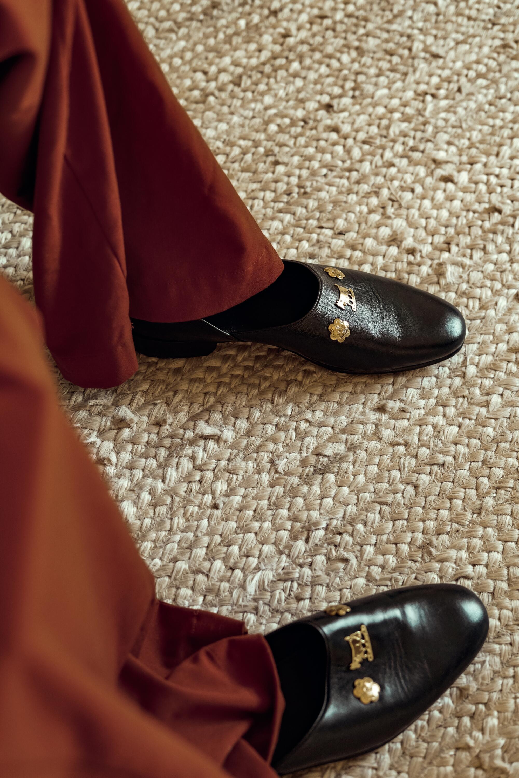 Photo of black Bode house shoes on carpet, red pants floating above