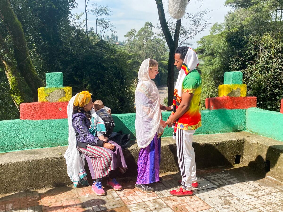 A man and woman stand holding hands while another person sits with a child