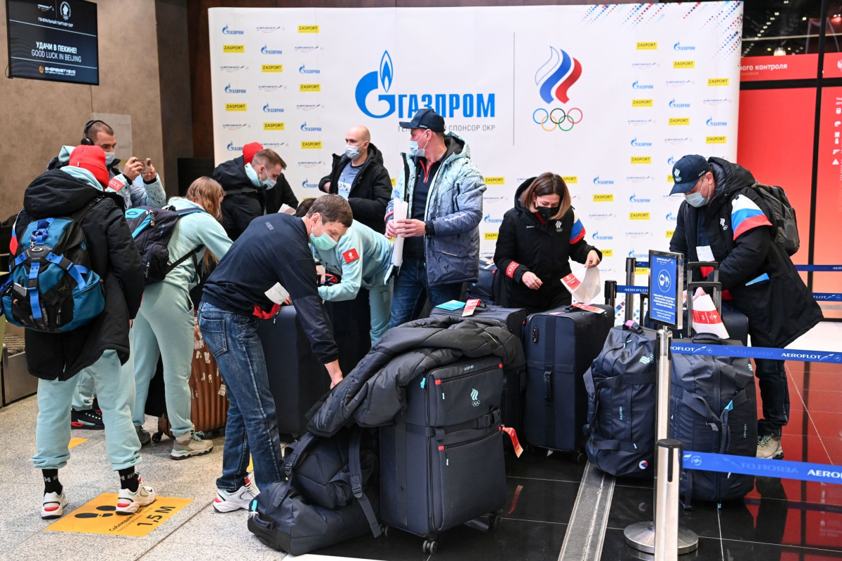 A group of people in masks stand amid piles of luggage inside an airport.