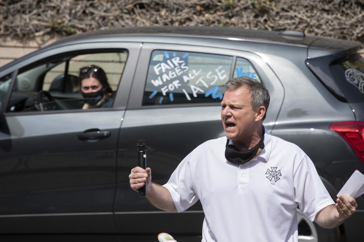 A man yells out. A car with "Fair wages for all IATSE" is in the background 