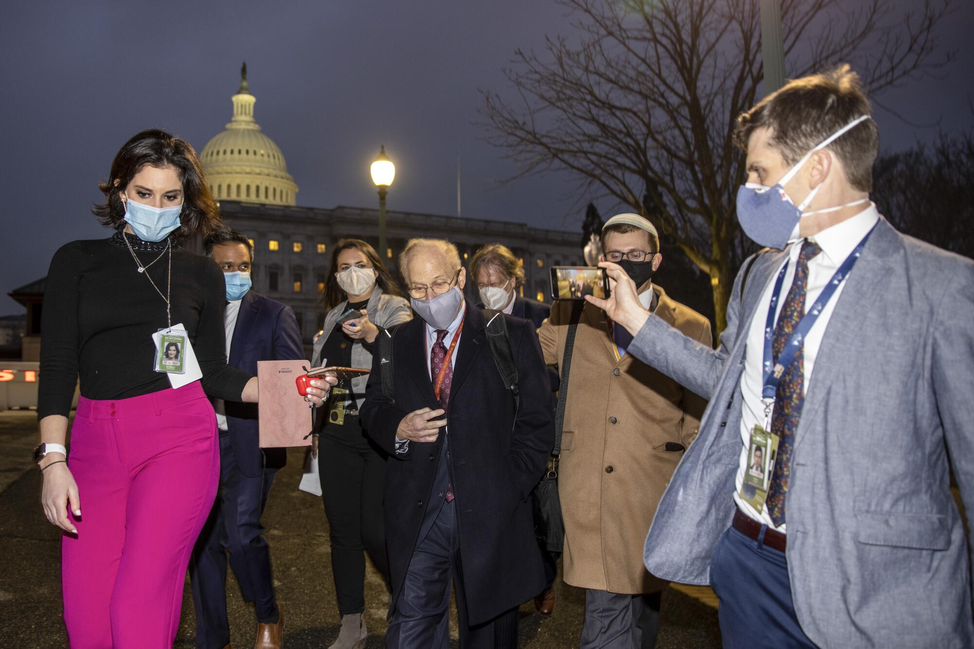 A group of people walk outside the Capitol at dusk