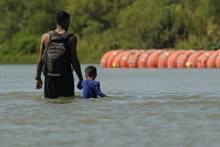 ARCHIVO - Migrantes caminan junto a grandes boyas que se utilizan como barrera fronteriza flotante en el río Bravo, el 1 de agosto de 2023, en Eagle Pass, Texas. (AP Foto/Eric Gay, Archivo)