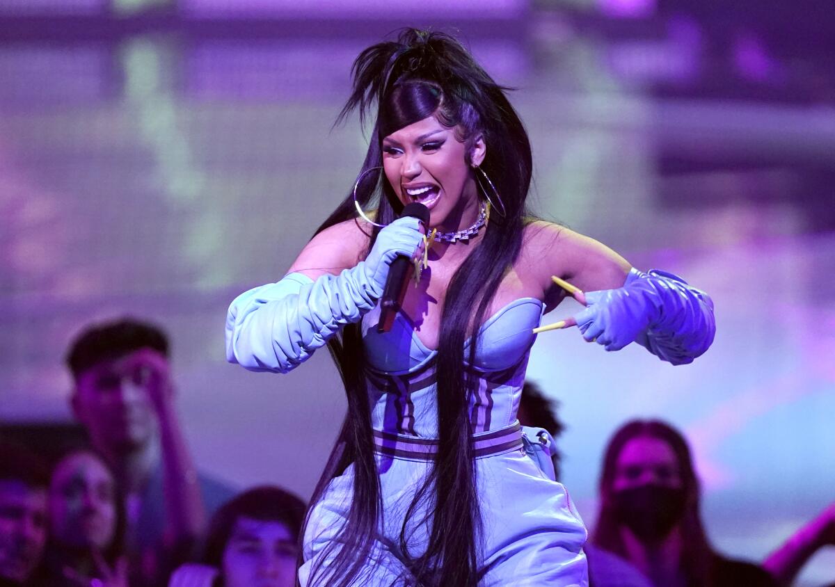 Cardi B performs onstage while wearing a light blue jumpsuit and large, gold hoop earrings.