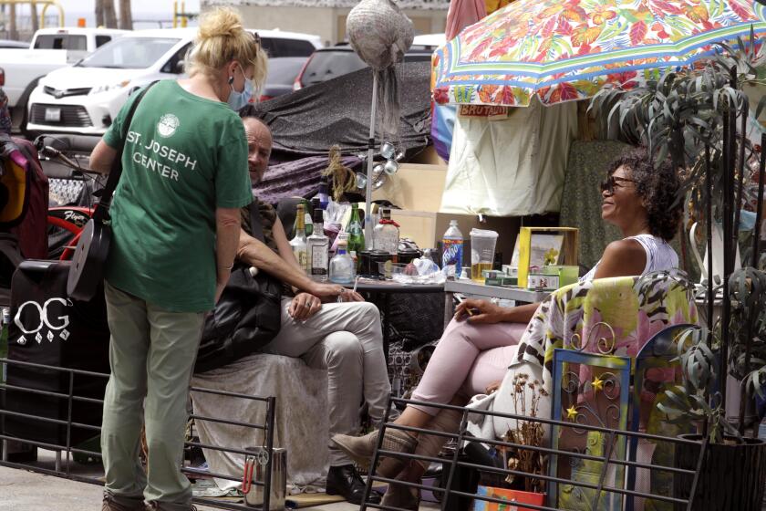 VENICE, CA - JULY 7, 2021 - - A worker with the St. Joseph Center talks with a homeless couple along Ocean Front Walk in Venice on July 7, 2021. St. Joseph Center, the lead agency in the encampment-to-housing program, have been trying to house the homeless living along the boardwalk in Venice. The organization reported last Friday that 72 people had left Ocean Front Walk, the concrete promenade commonly known as the boardwalk, and the earthen berm next to it where about 200 tents had accumulated. The initial effort concentrated on tents scattered over the south end of the boardwalk between Windward Avenue and Park Court. Security officers, with City of Los Angeles Recreation and Parks, have been placing notices warning homeless of a clean-up happening on July 9. The notice said, "All items that pose an immediate threat to the health or safety of the public may be immediately removed and discarded. (Genaro Molina / Los Angeles Times)