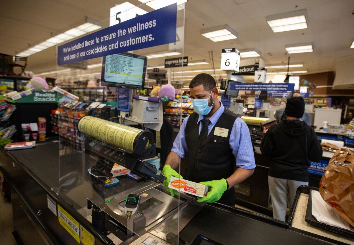 Everardo Gonzalez scans groceries behind a new plexiglass barrier at a Ralphs grocery store in Marina Del Rey during the coronavirus pandemic on Sunday.